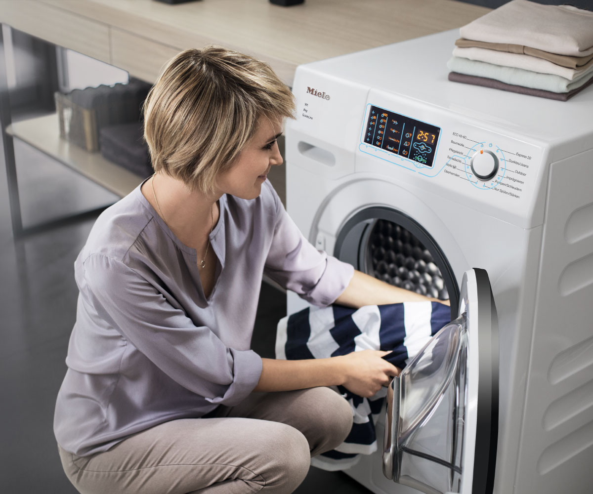 Eine Dame belädt die Waschmaschine mit einem Wäschestück.